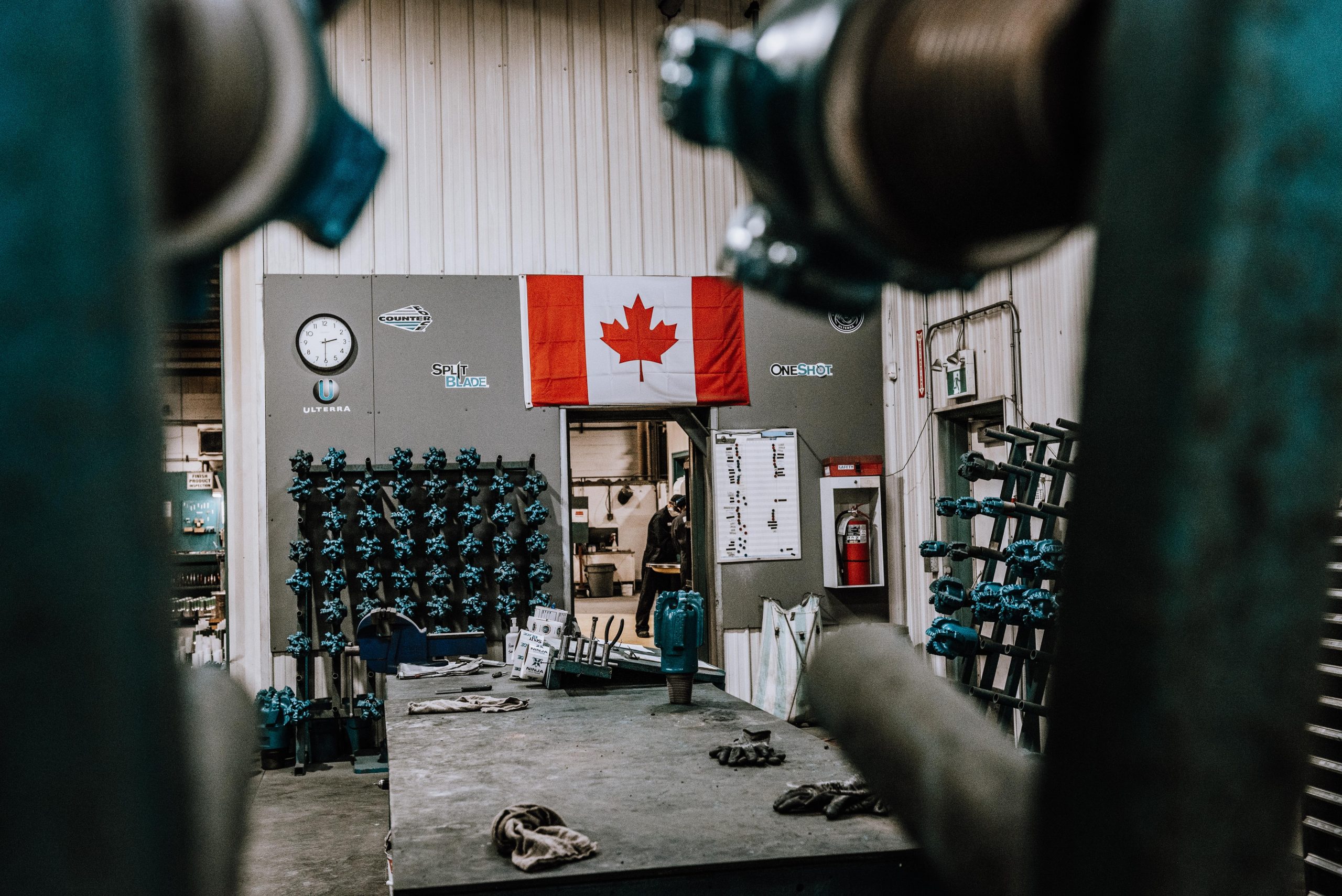 View of an Ulterra workshop with a Canadian flag and completed high-ROP HOG PDC bits on a wall